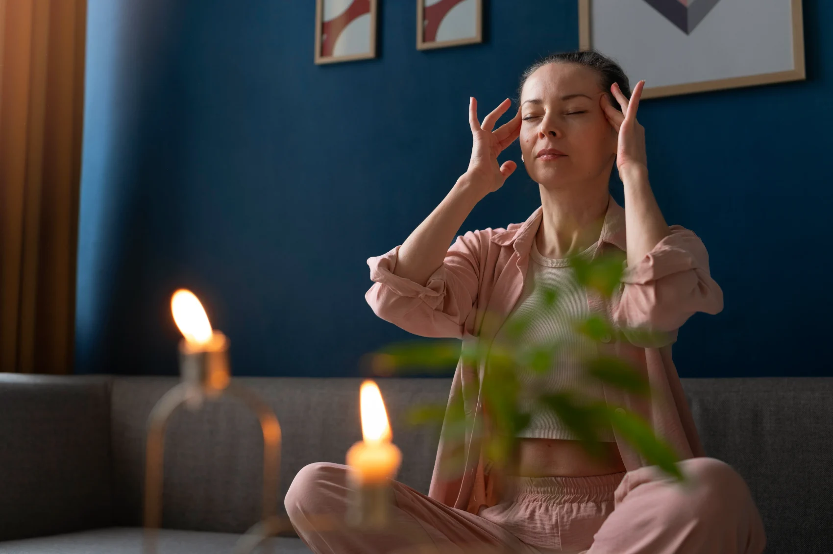 A person sitting cross-legged with eyes closed and fingertips at the temples, quietly noticing an emotional response