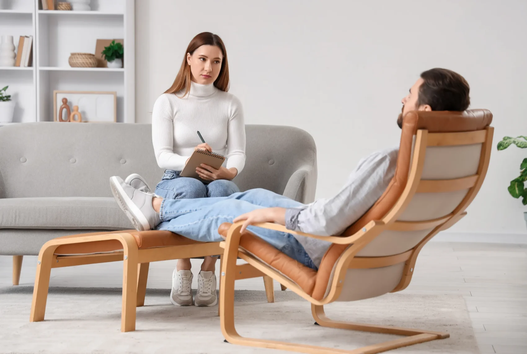 A practitioner taking notes while a client rests comfortably in a reclining chair during an initial therapeutic conversation