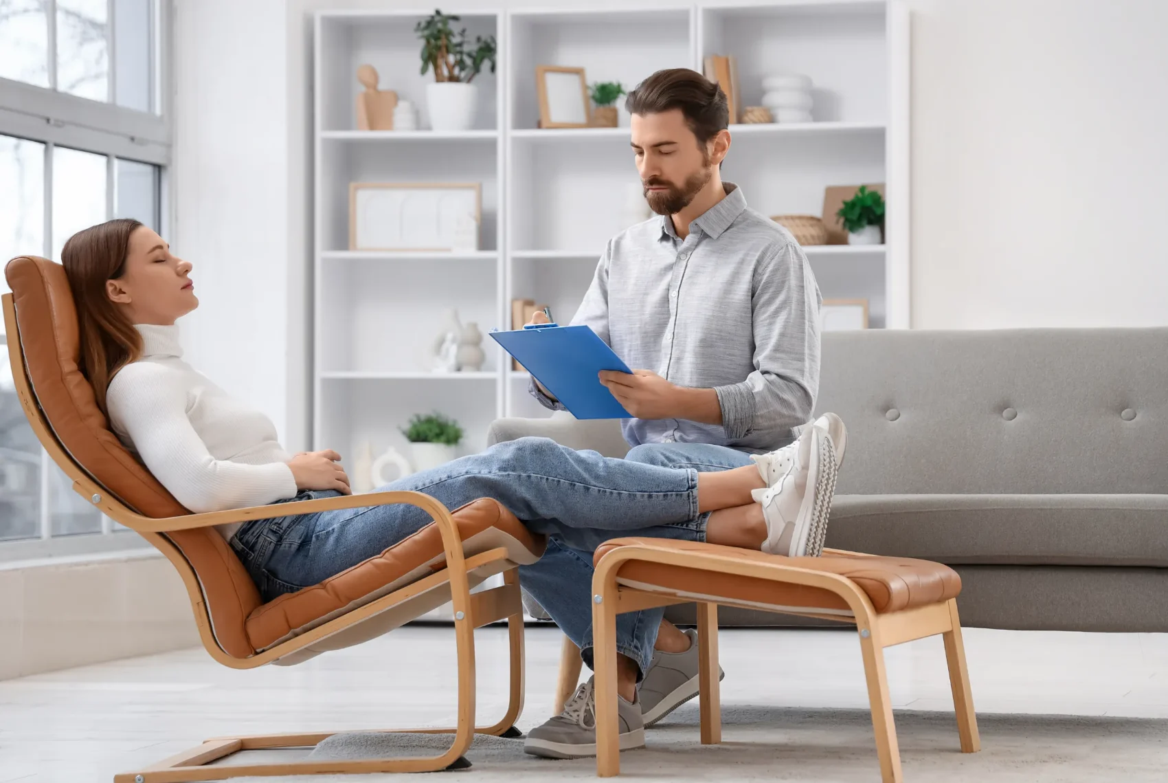 A regression therapy practitioner sitting beside a client who is resting comfortably in a reclining chair